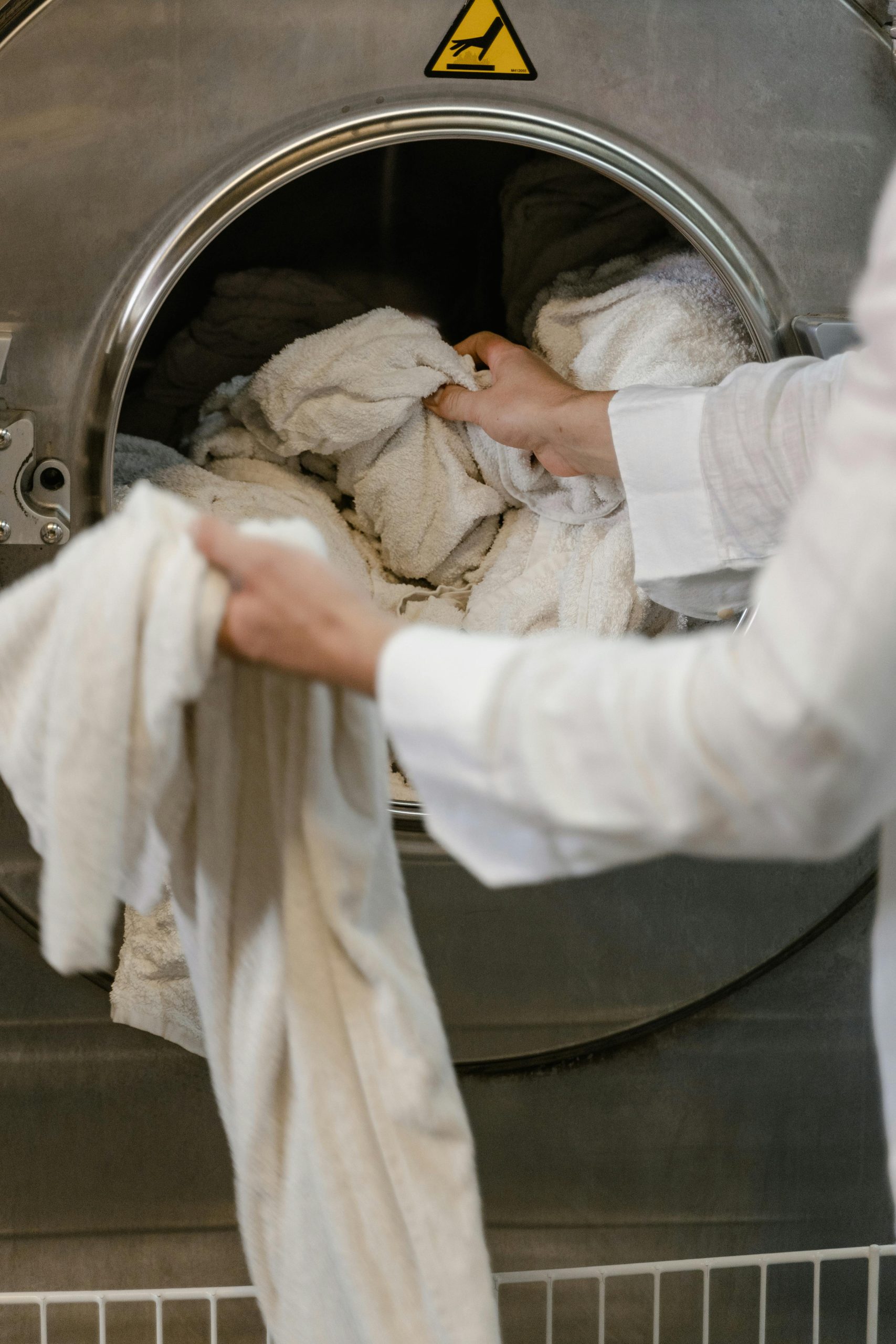 A person loading towels into an industrial washing machine in a launderette.